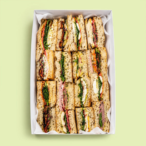 Assorted focaccia sandwiches in a box on a light green background for office catering