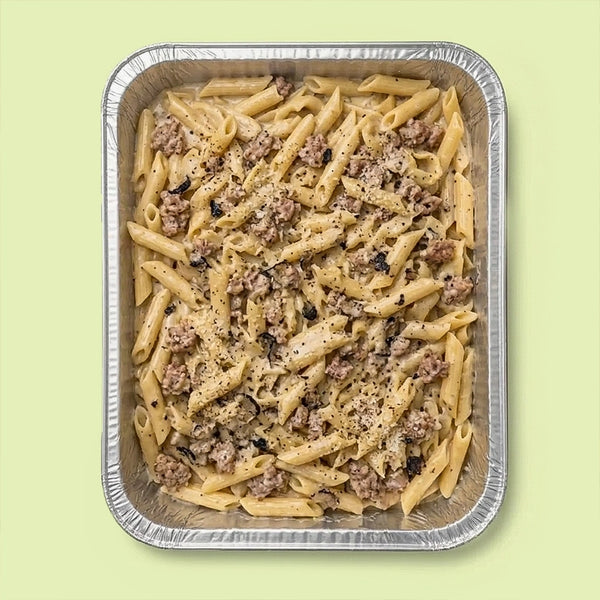 Penne pasta with pork sausage meat, cream and truffle in a foil tray on a light green background