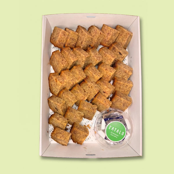 Box of banana bread bites with a small container of butter labeled 'Eatalo' on a light green background