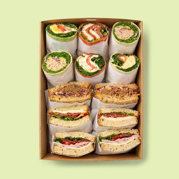 Box of assorted sandwiches and wraps on a light green background for office catering