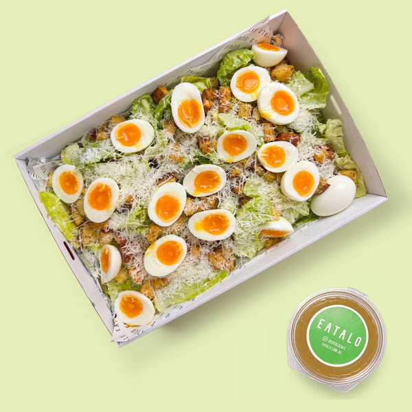 Box of salad with boiled eggs and croutons on a light green background, featuring the brand 'Eatalo'.