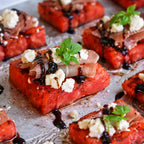 Plated dish of watermelon slices topped with feta, prosciutto, and mint on a metal tray. Perfect bites and canapé for Morning and afternoon Tea