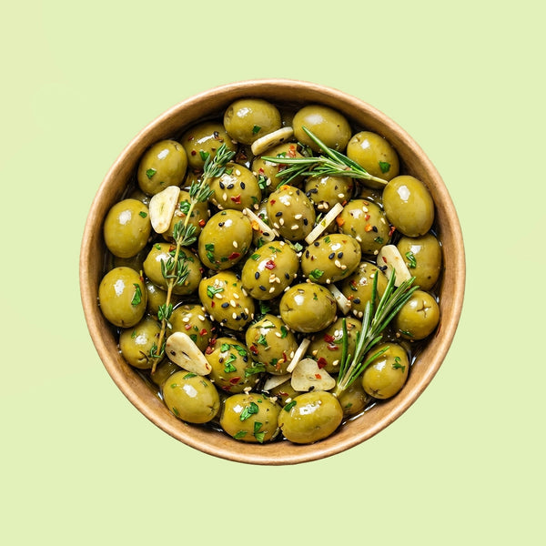 Bowl of marinated green cocktail olives with herbs on a light green background