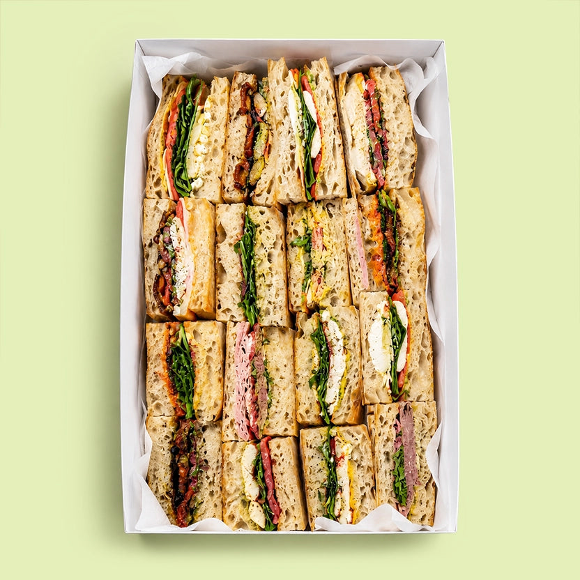 Assorted focaccia sandwiches in a box on a light green background for office catering