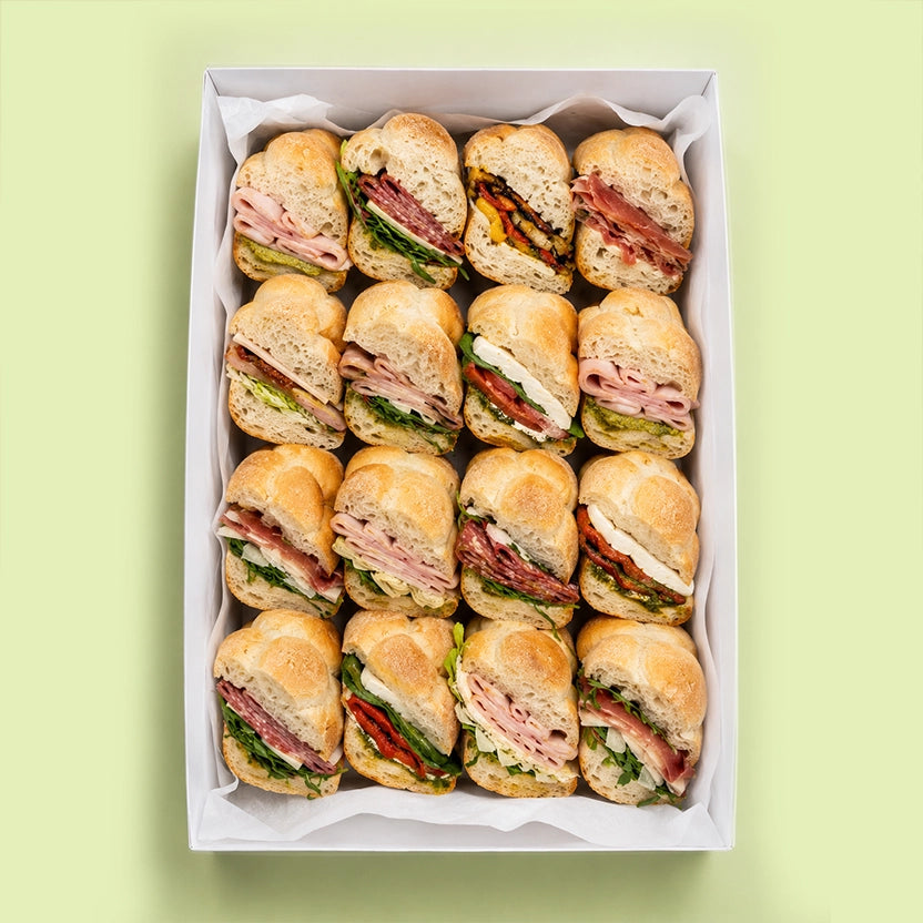 Box of sliced rosetta roll sandwiches on a light green background