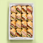 Box of sliced rosetta roll sandwiches on a light green background