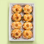 Box of rosetta roll sandwiches with buns on a light green background for office catering with mix assortment.