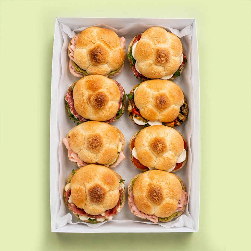 Box of rosetta roll sandwiches with buns on a light green background for office catering with mix assortment.
