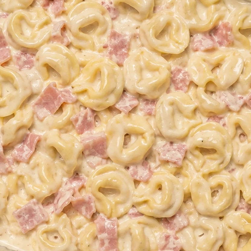 Close-up of creamy tortellini pasta with ham pieces and cream