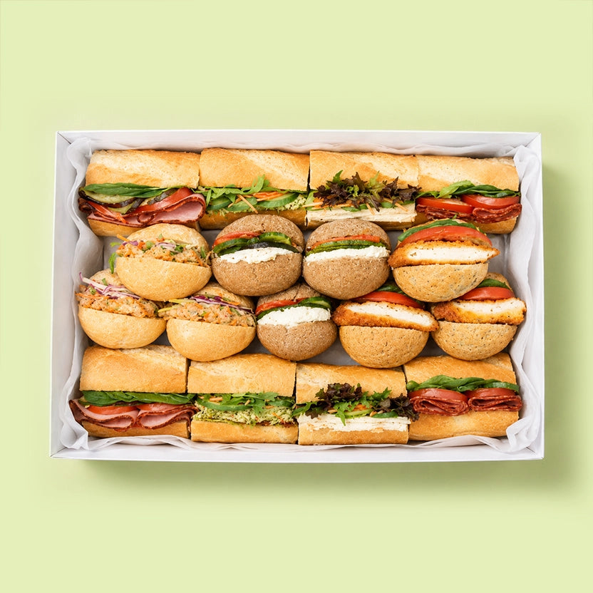 Assorted baguette sandwiches in a box on a light green background for office catering