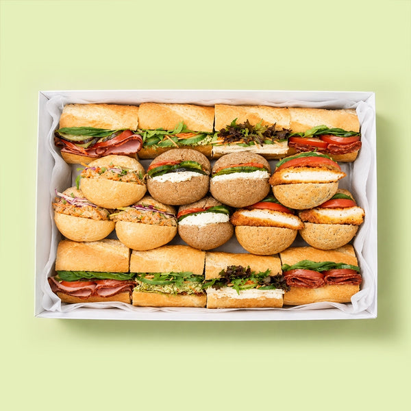 Assorted baguette sandwiches in a box on a light green background for office catering