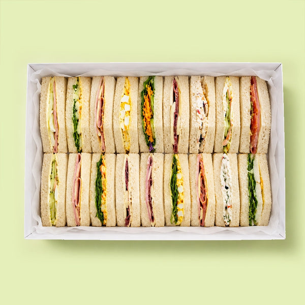 Box of assorted mini finger triangle sandwiches on a light green background