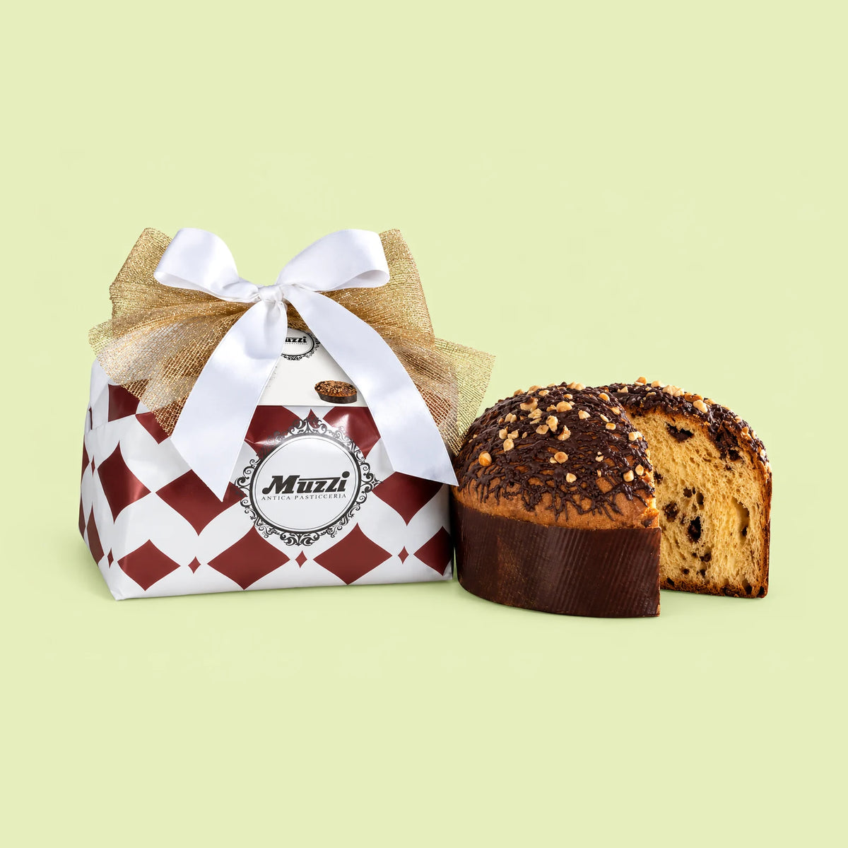A packaged slice of Muzzi Panettone displayed next to its gift box on a pale yellow-green background. The box is white and burgundy with a red harlequin pattern, decorated with a white satin bow, a gold mesh ribbon, and a central round logo medallion reading 'Muzi'.