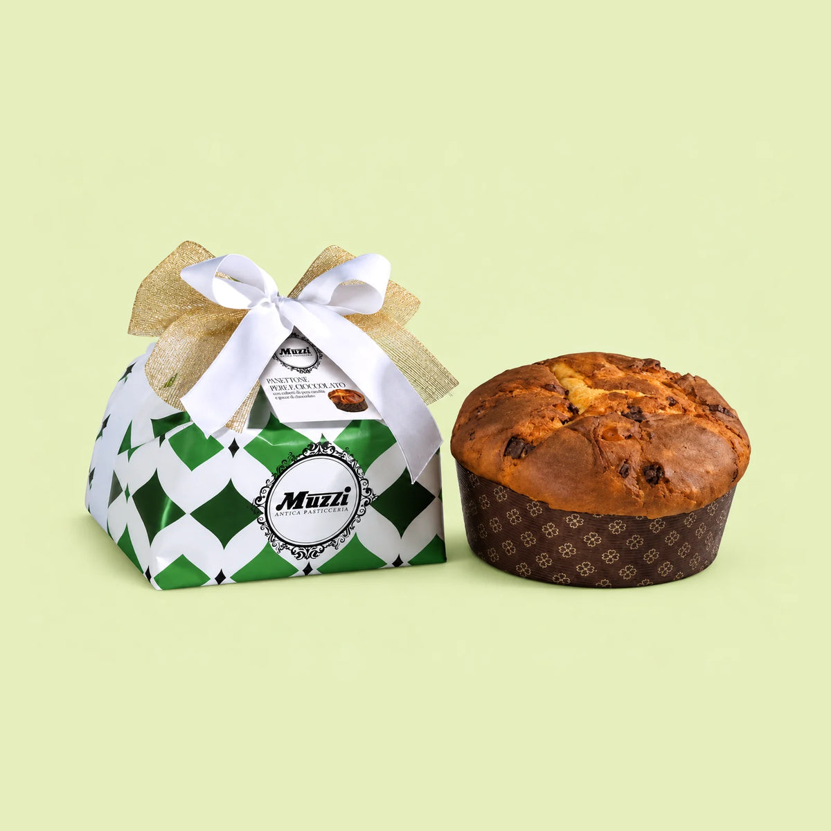 A Muzzi Pear and Chocolate Panettone cake shown next to its decorated gift box on a solid pale yellow-green background. The box is white and green with a diamond pattern and tied with a white ribbon and gold bow.