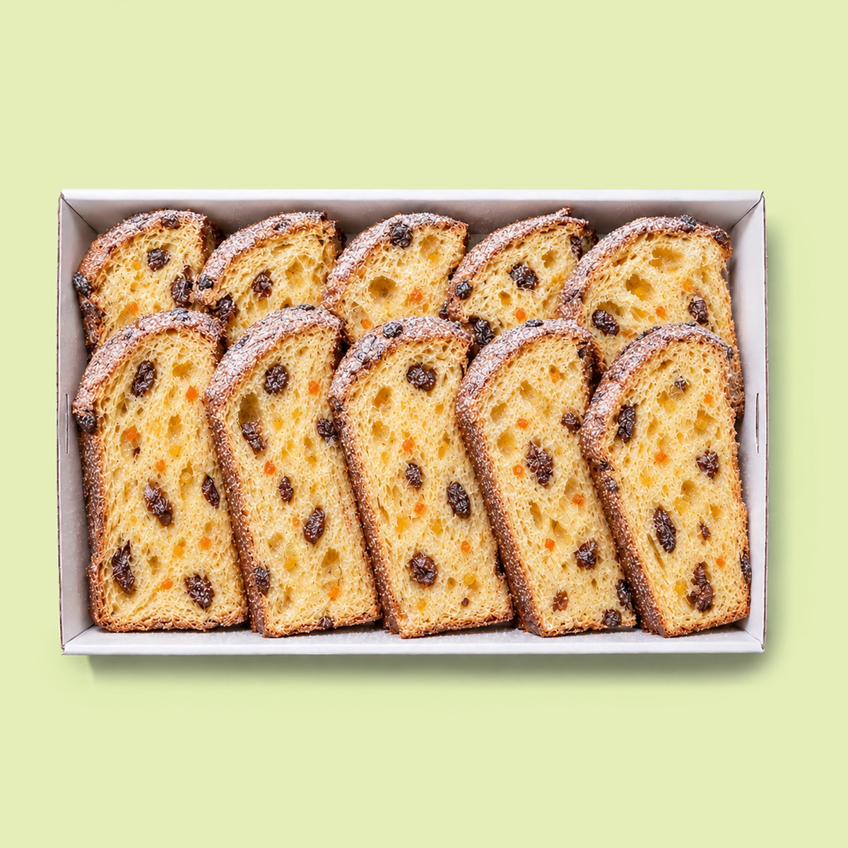 Panettone platter in a white catering box with ten thick slices of panettone, raisins and candied orange peel, on a pale green background.