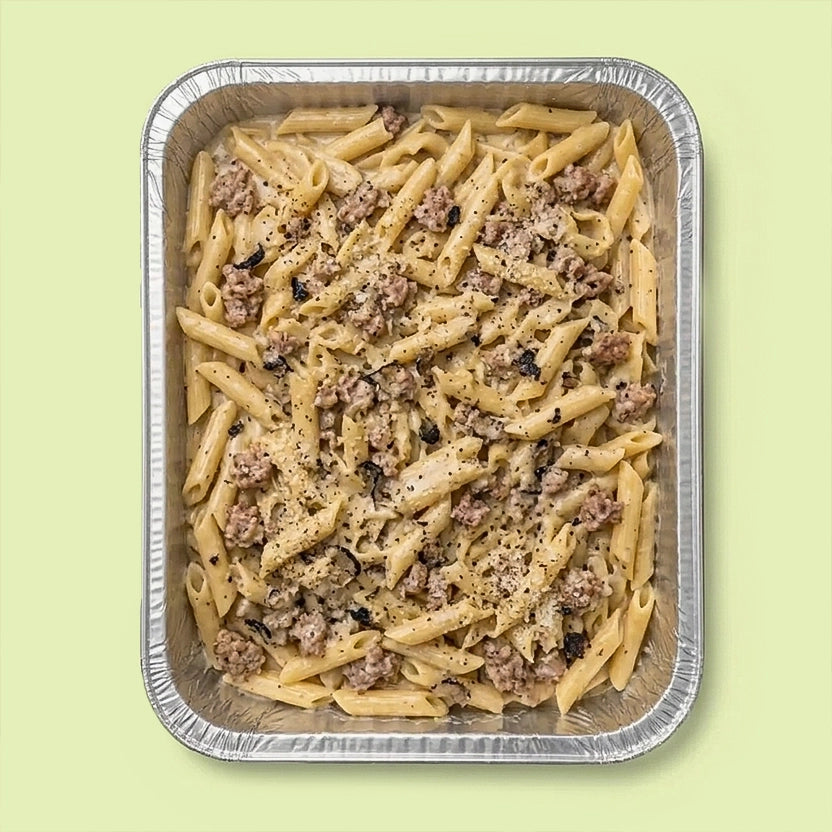 Penne pasta with pork sausage meat, cream and truffle in a foil tray on a light green background