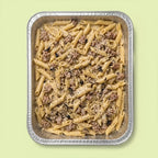 Penne pasta with pork sausage meat, cream and truffle in a foil tray on a light green background