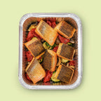 Top-down view of EATALO’s crispy-skin roast salmon platter with roasted vegetables in a catering tray on a light pink background.
