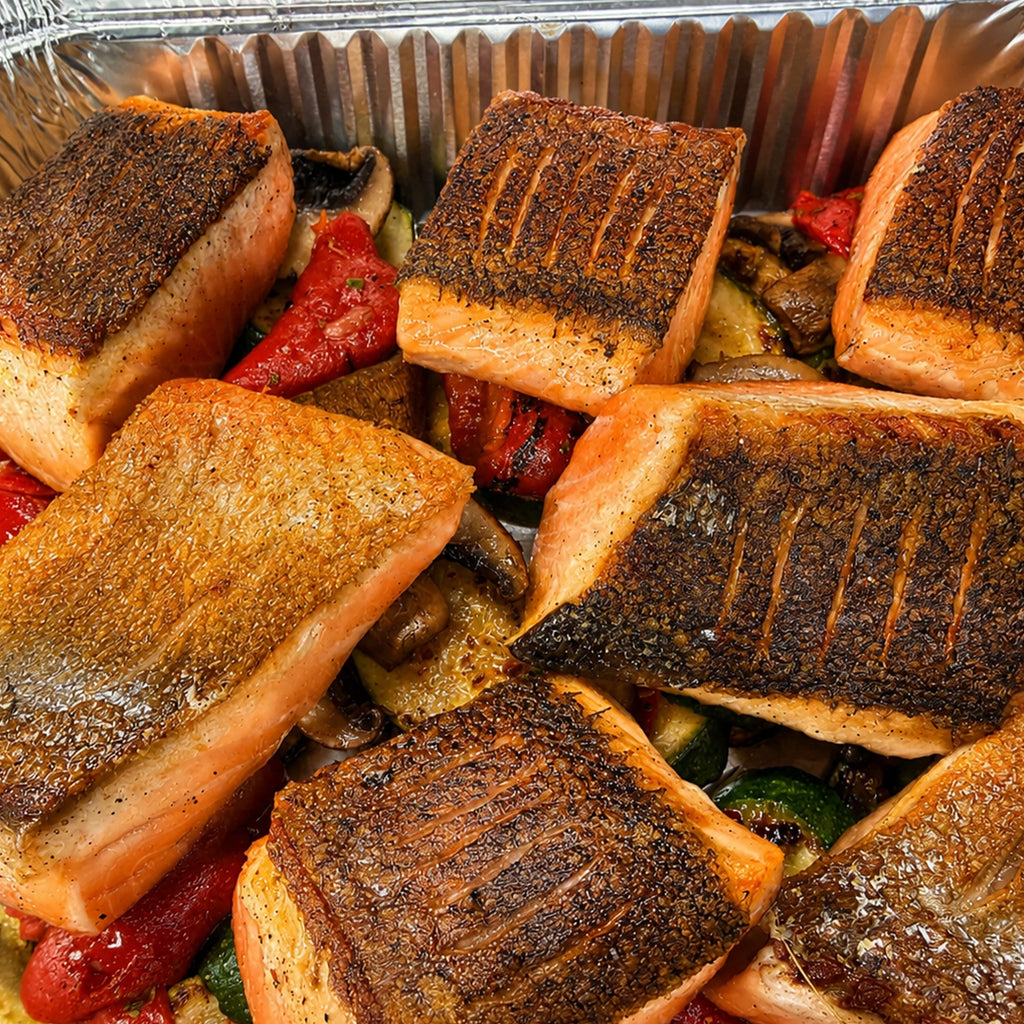 Close-up of crispy-skin roasted salmon pieces served over marinated vegetables in EATALO’s premium catering platter.
