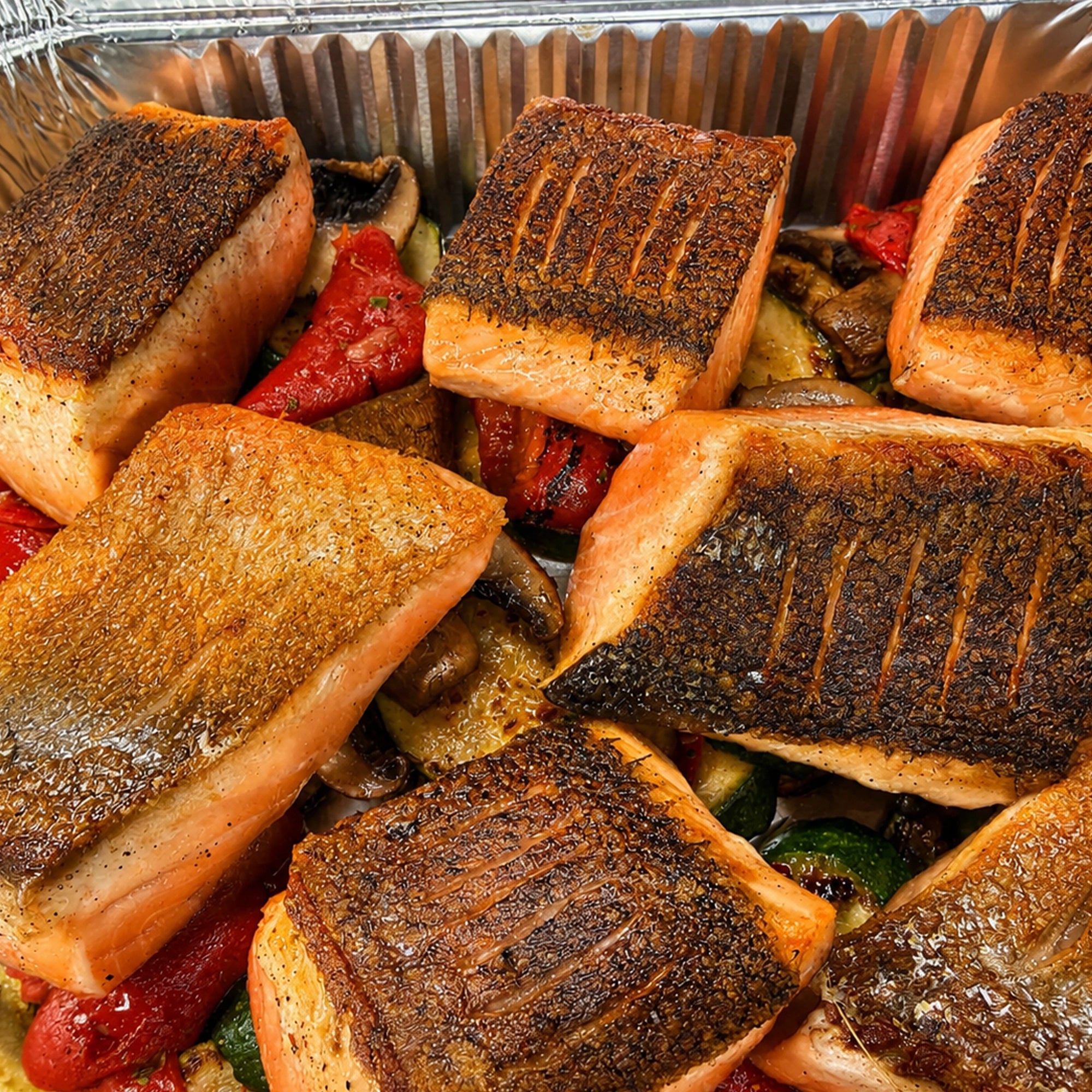 Close-up of crispy-skin roasted salmon pieces served over marinated vegetables in EATALO’s premium catering platter.
