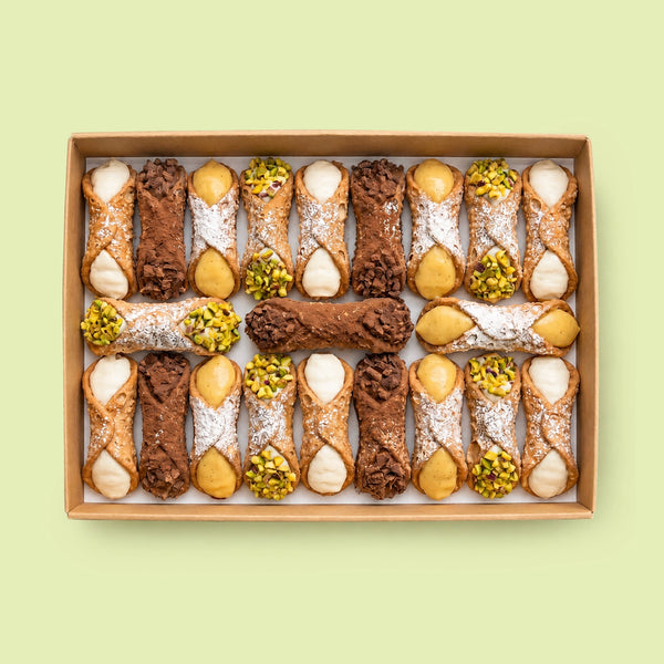 Assorted Italian Cannoli pastries in a box on a light green background