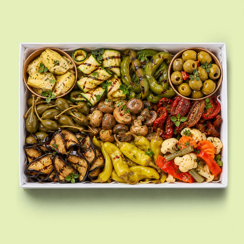 Marinated vegetables antipasto platter in a white box with artichoke hearts, grilled zucchini, capsicum, roasted eggplant, sautéed mushrooms, caperberries, banana peppers, sun-dried tomatoes, pickled cauliflower and Castelvetrano olives.