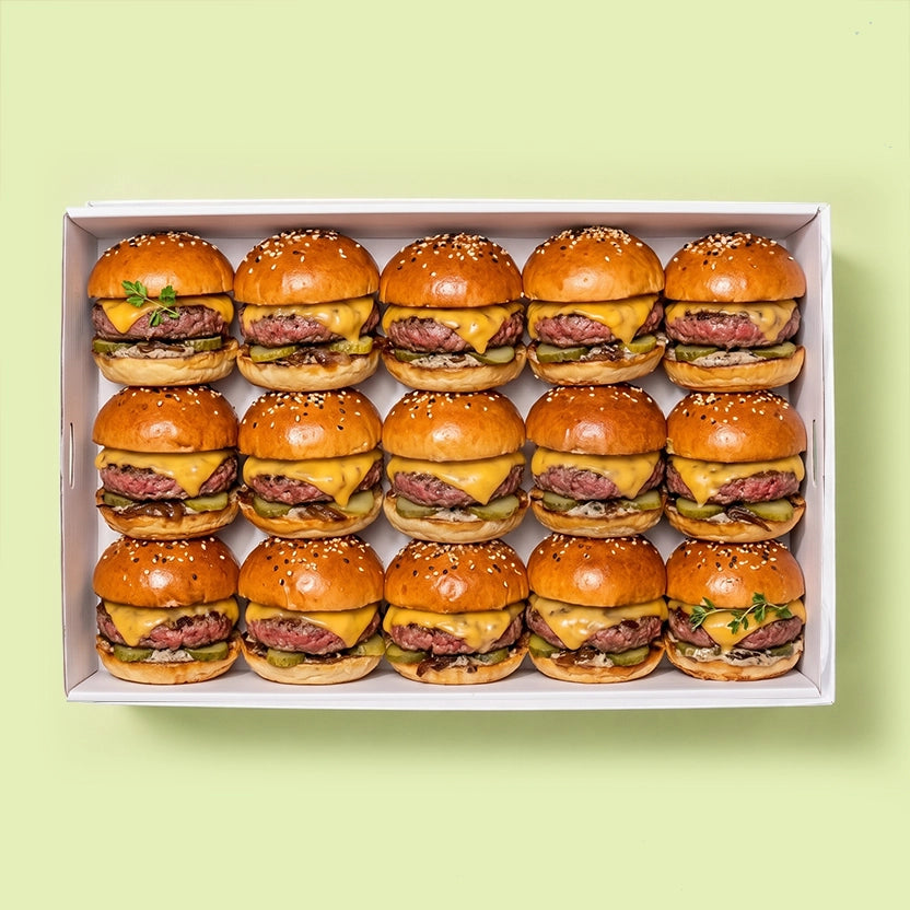 Tray of 15 mini cheeseburger sliders with beef patty, melted cheddar cheese and pickle on a sesame seed bun.
