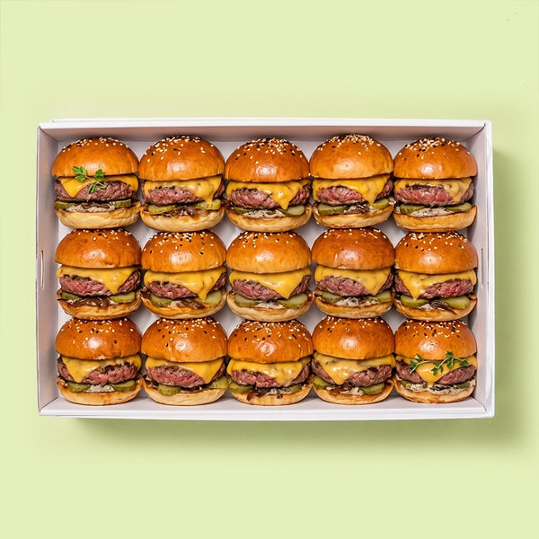 Tray of 15 mini cheeseburger sliders with beef patty, melted cheddar cheese and pickle on a sesame seed bun.