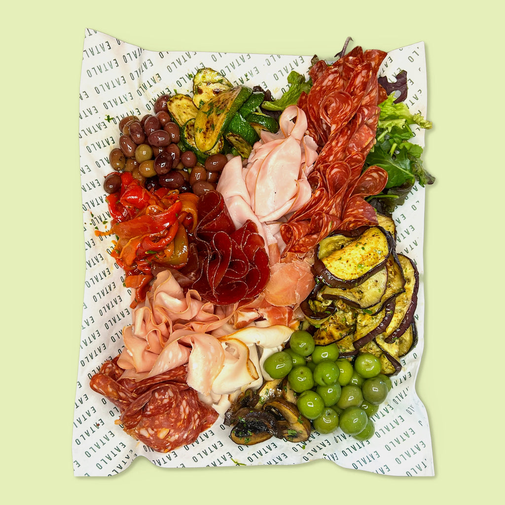Platter of cured meats, cheeses, and vegetables on a patterned paper background