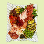 Platter of cured meats, cheeses, and vegetables on a patterned paper background