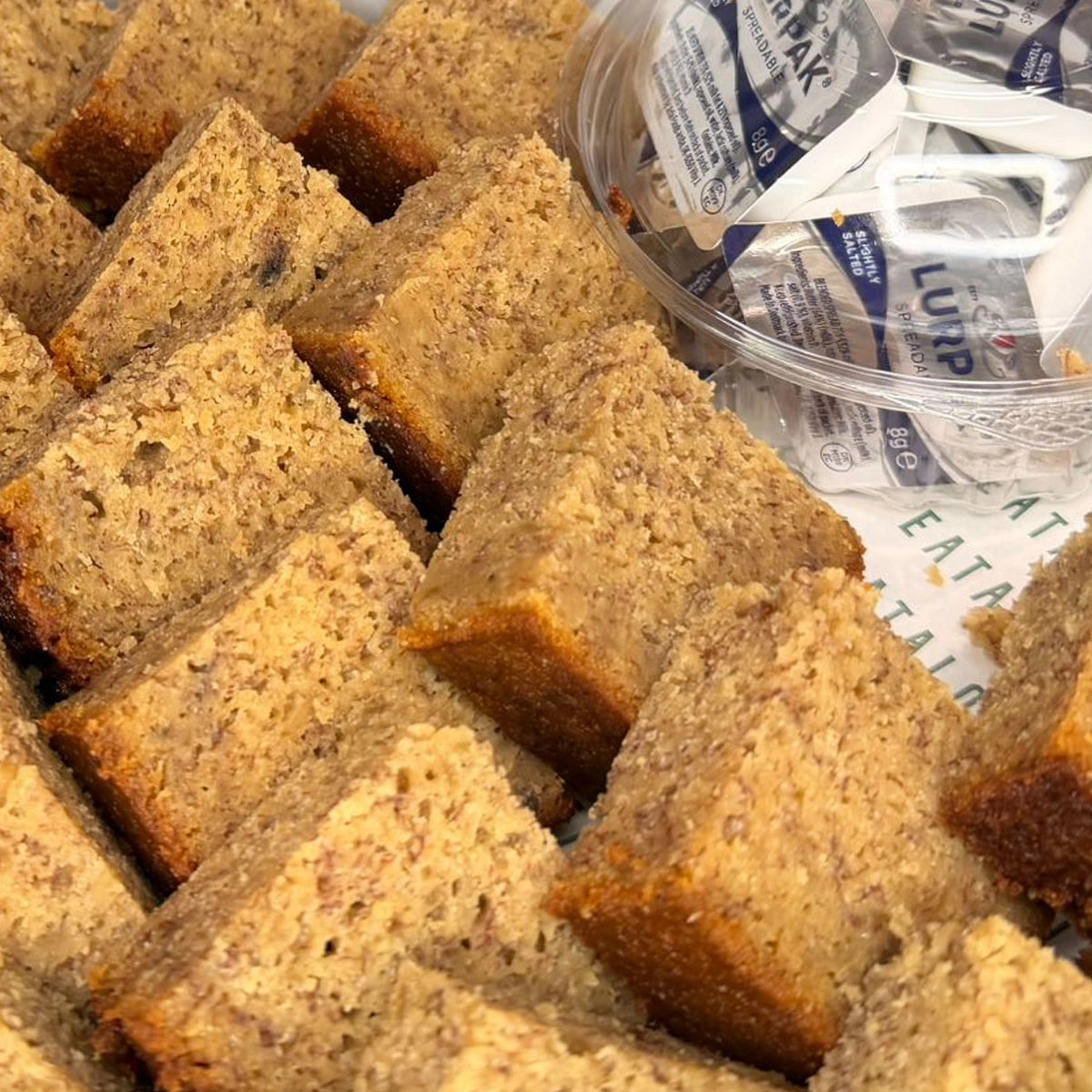 Banana Bread cubes with a container of butter spread on a paper bag background