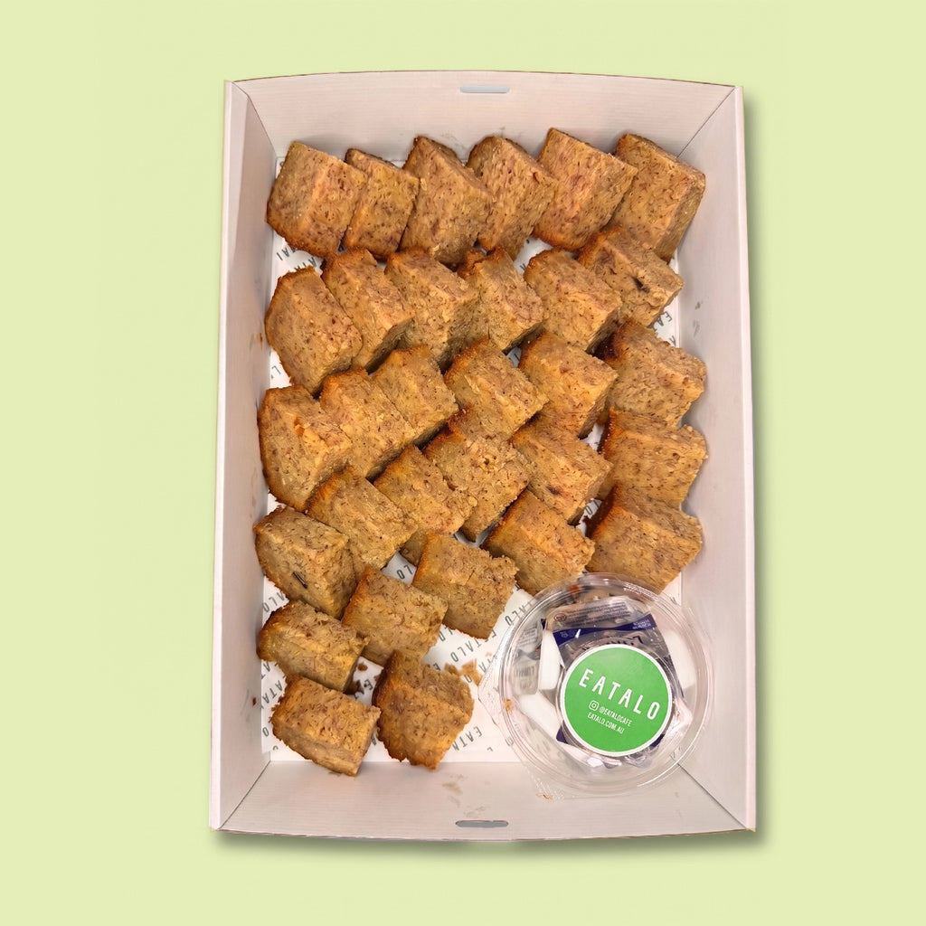 Box of banana bread bites with a small container of butter labeled 'Eatalo' on a light green background