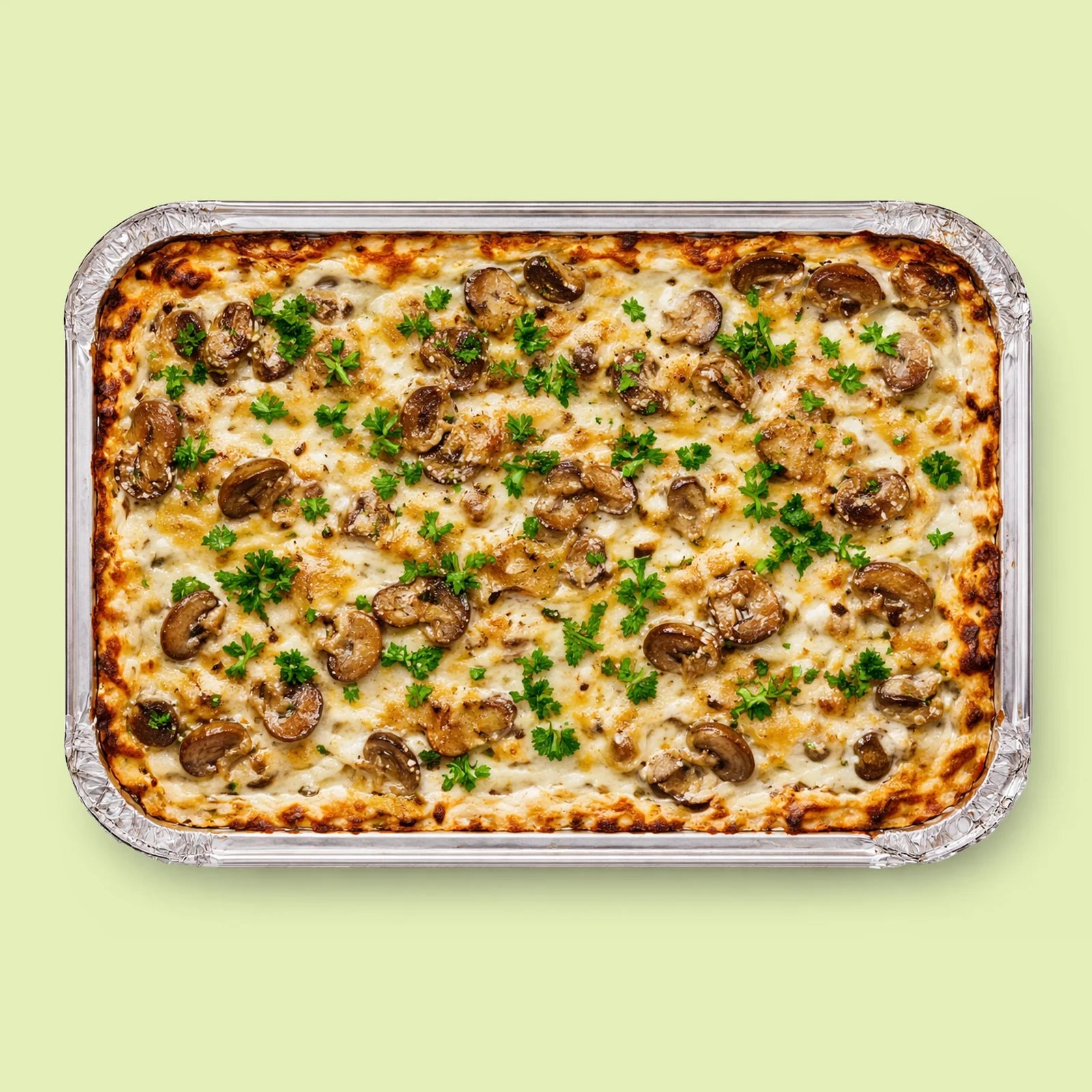 Baked lasagna with mushrooms and herbs in a foil tray on a light green background