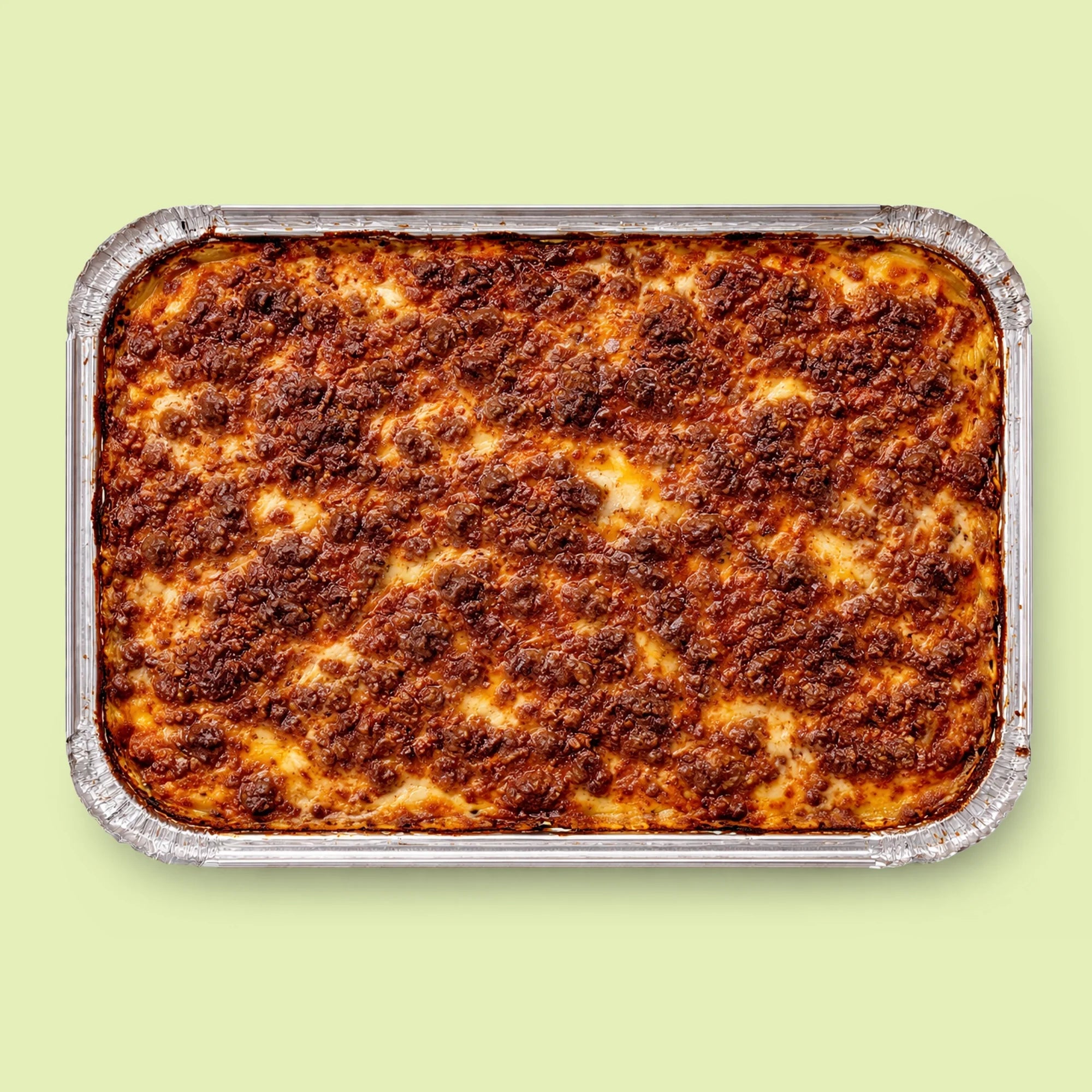 Baked lasagna in a foil tray on a light green background
