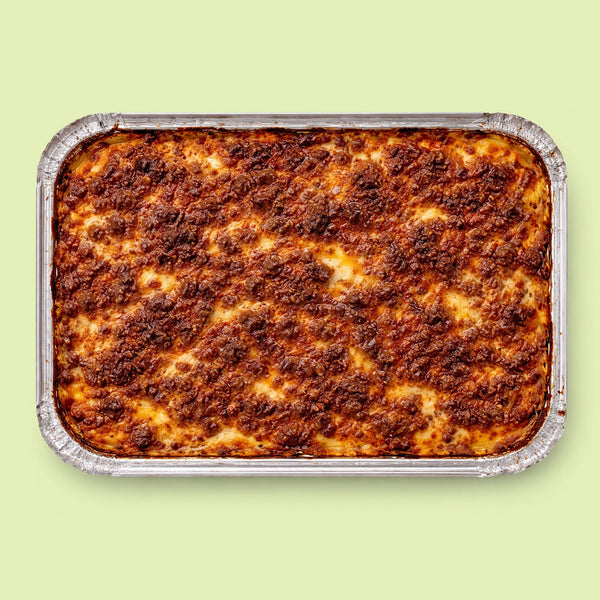 Baked lasagna in a foil tray on a light green background