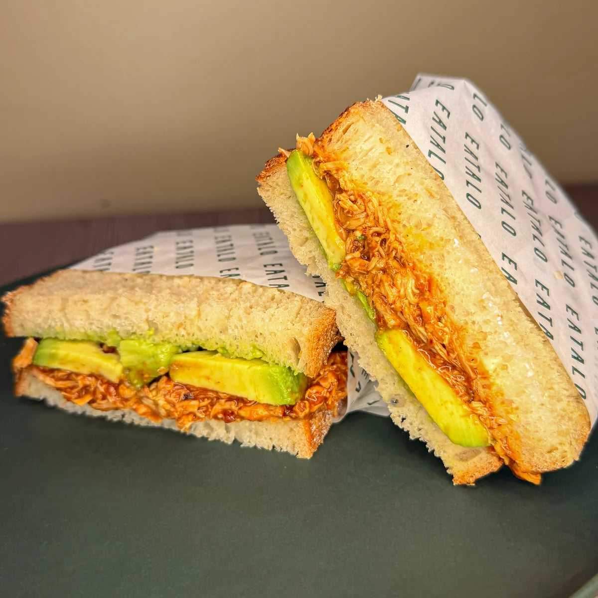 Sandwich with avocado and chicken on a plate with branded paper for catering in Sydney.