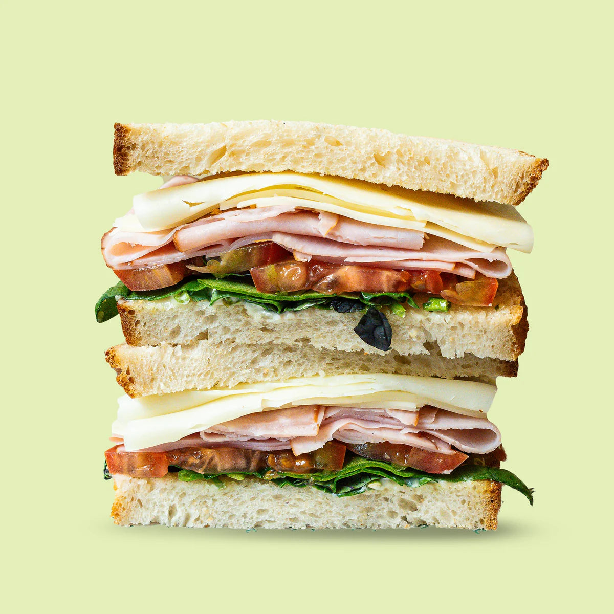 Deli sandwich with ham, cheese, lettuce, and tomato on a light green background