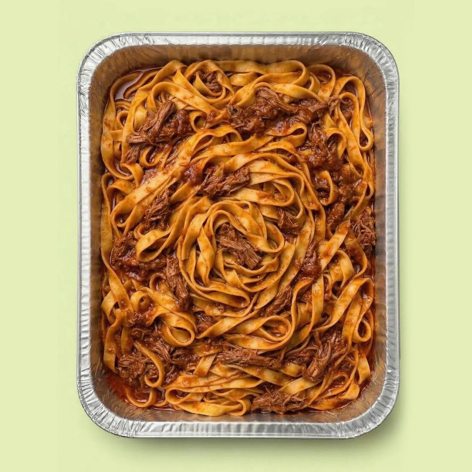 Aluminum tray with tagliatelle pasta and slow-cooked lamb ragù sauce on a light green background