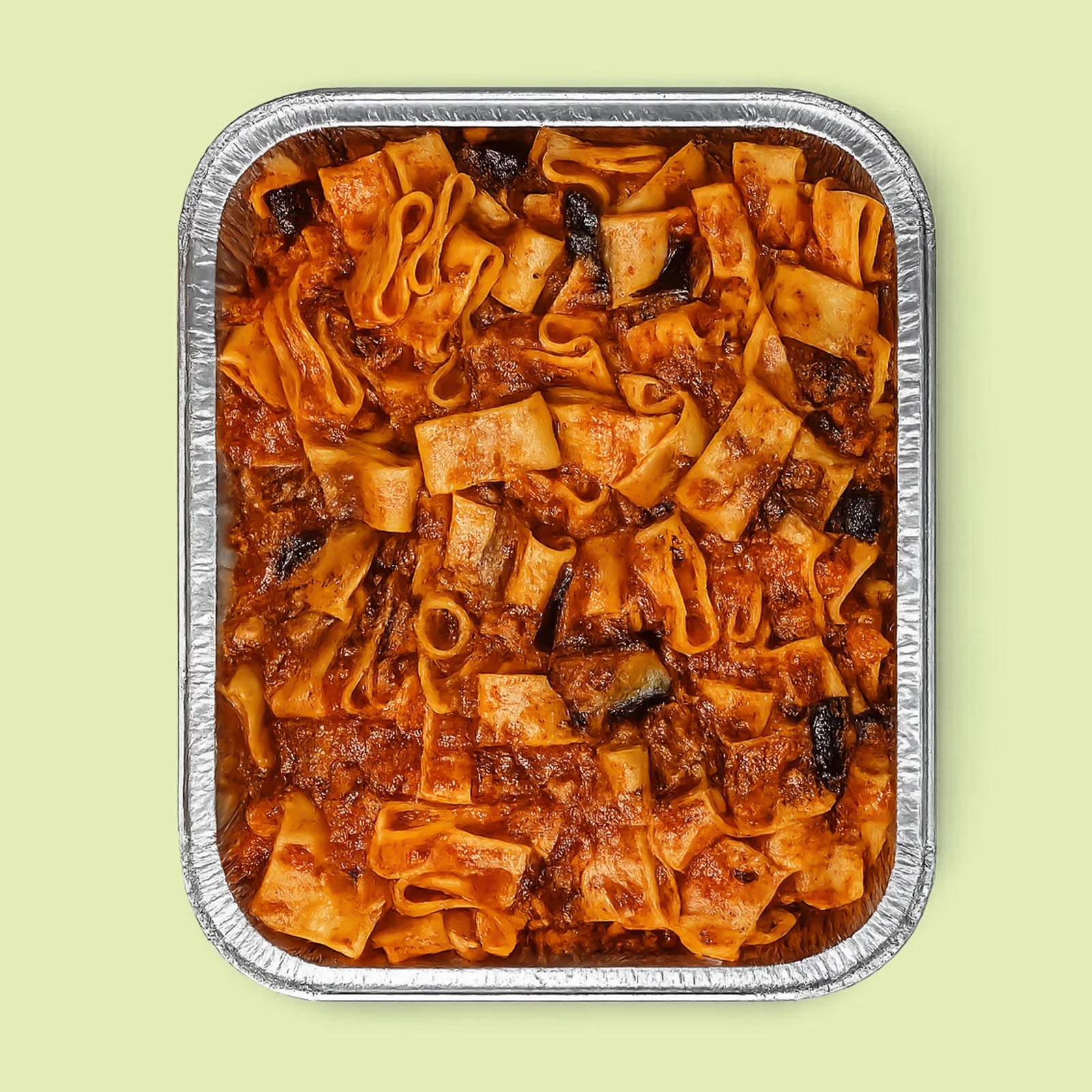 Foil-tray of pasta dish with oxtail beef sauce and eggplants on a light green background