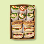 Box of assorted sandwiches and wraps on a light green background for office catering