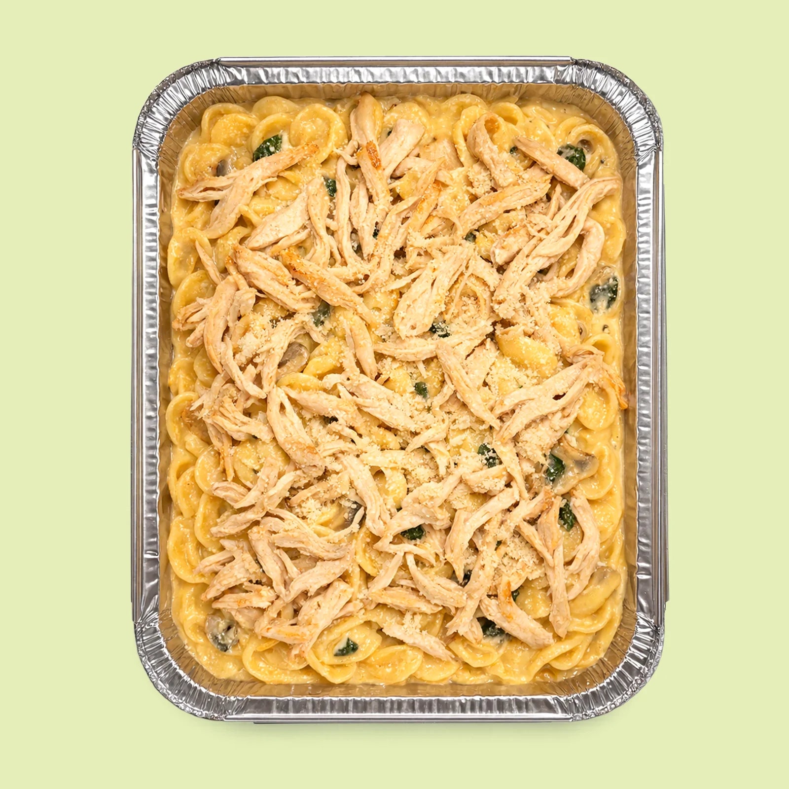 Foil-tray of orecchiette italian pasta with chicken, parmesan and herbs on a light green background