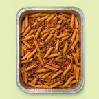 Foil pan with penne pasta and meat sauce bolognese on a light green background