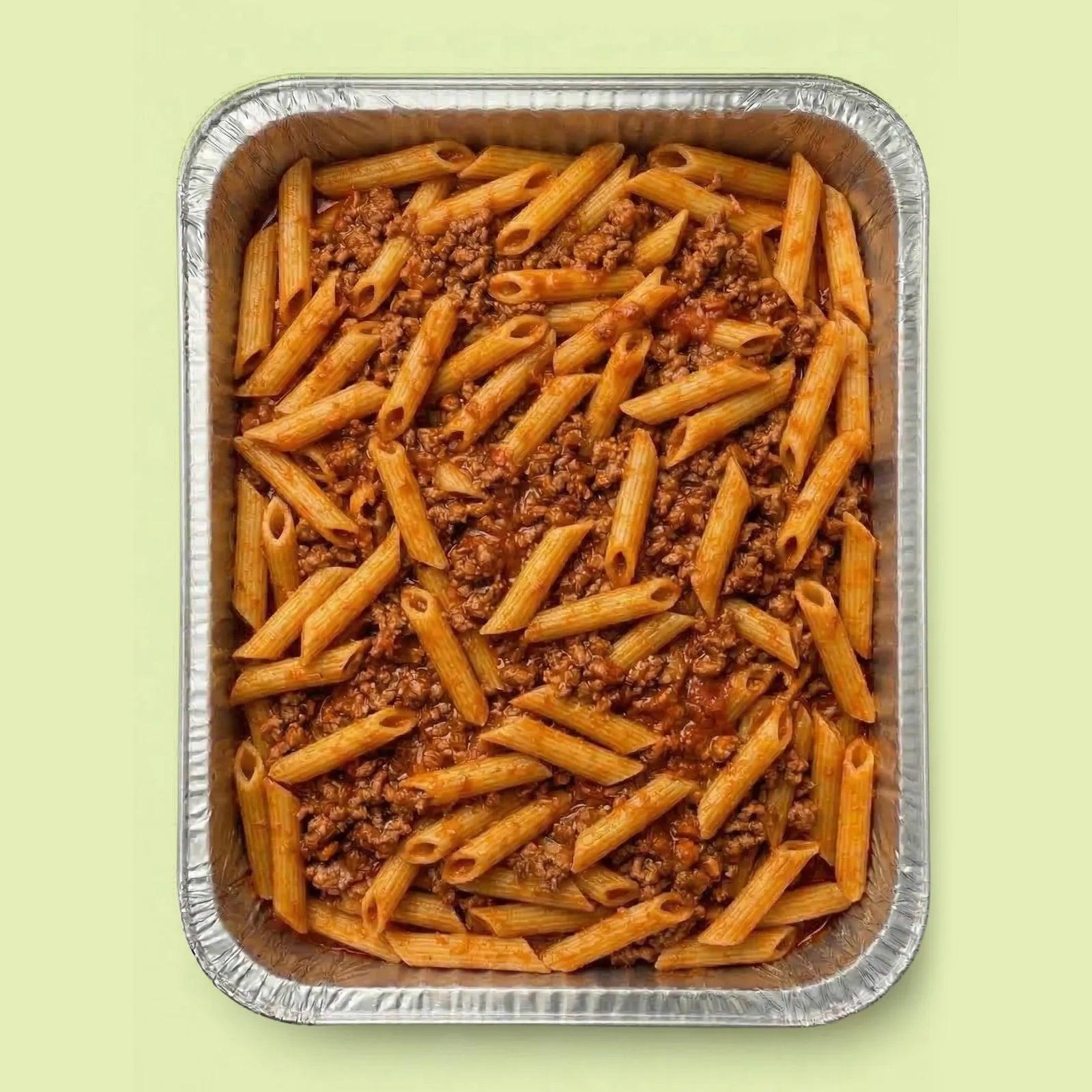 Foil pan with penne pasta and meat sauce bolognese on a light green background