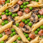 Italian pasta dish with penne, peas, mushrooms, and pieces of ham in a creamy sauce.