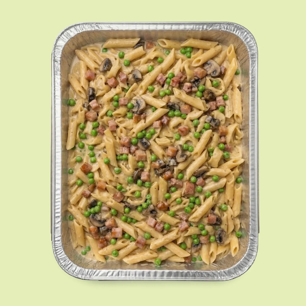 Italian pasta dish with peas and mushrooms in a metal tray on a light green background