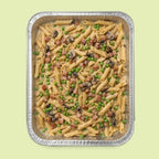 Italian pasta dish with peas and mushrooms in a metal tray on a light green background