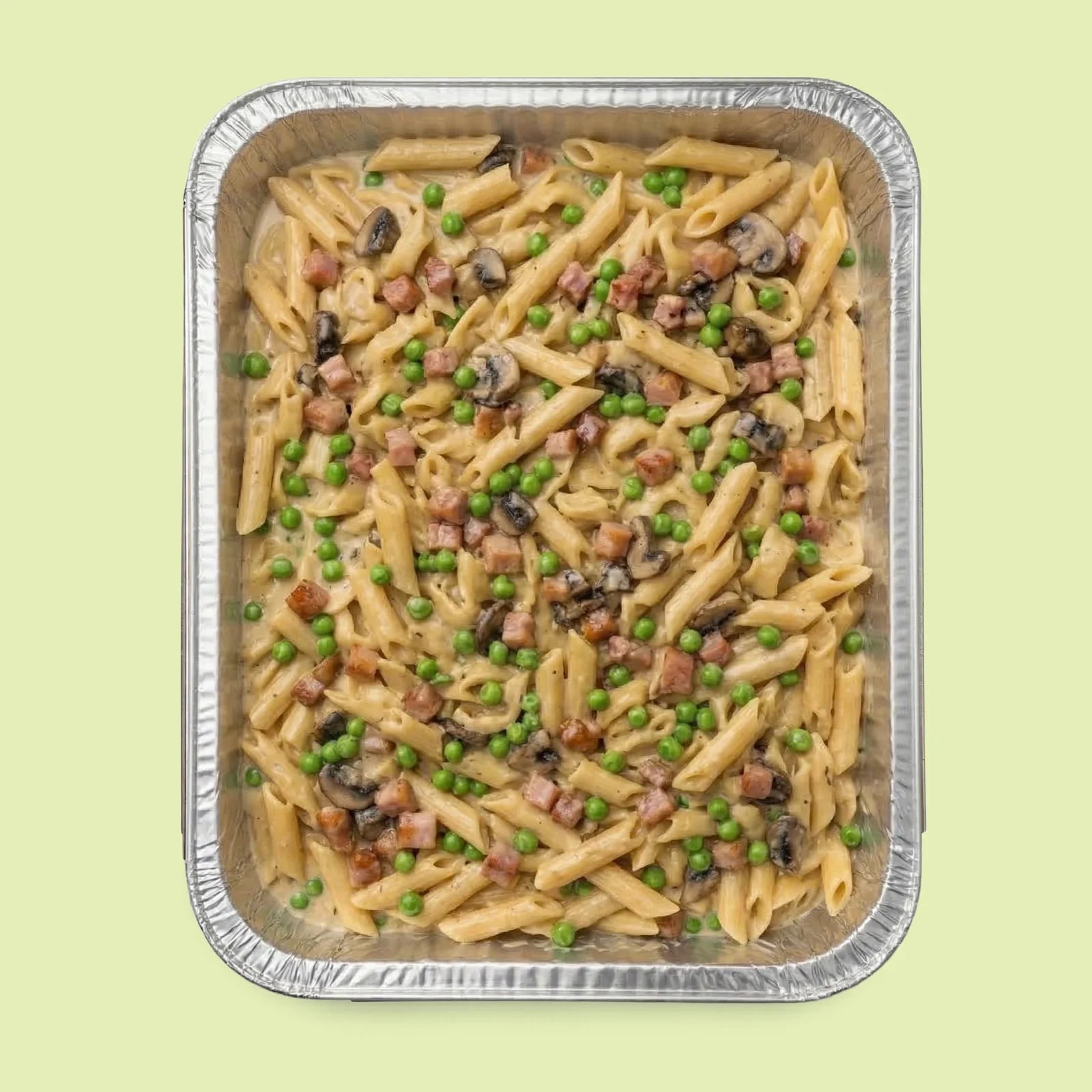 Italian pasta dish with peas and mushrooms in a metal tray on a light green background