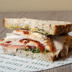 Half-cut sandwich with visible layers of bread, turkey, pesto, and rocket on a wooden surface.