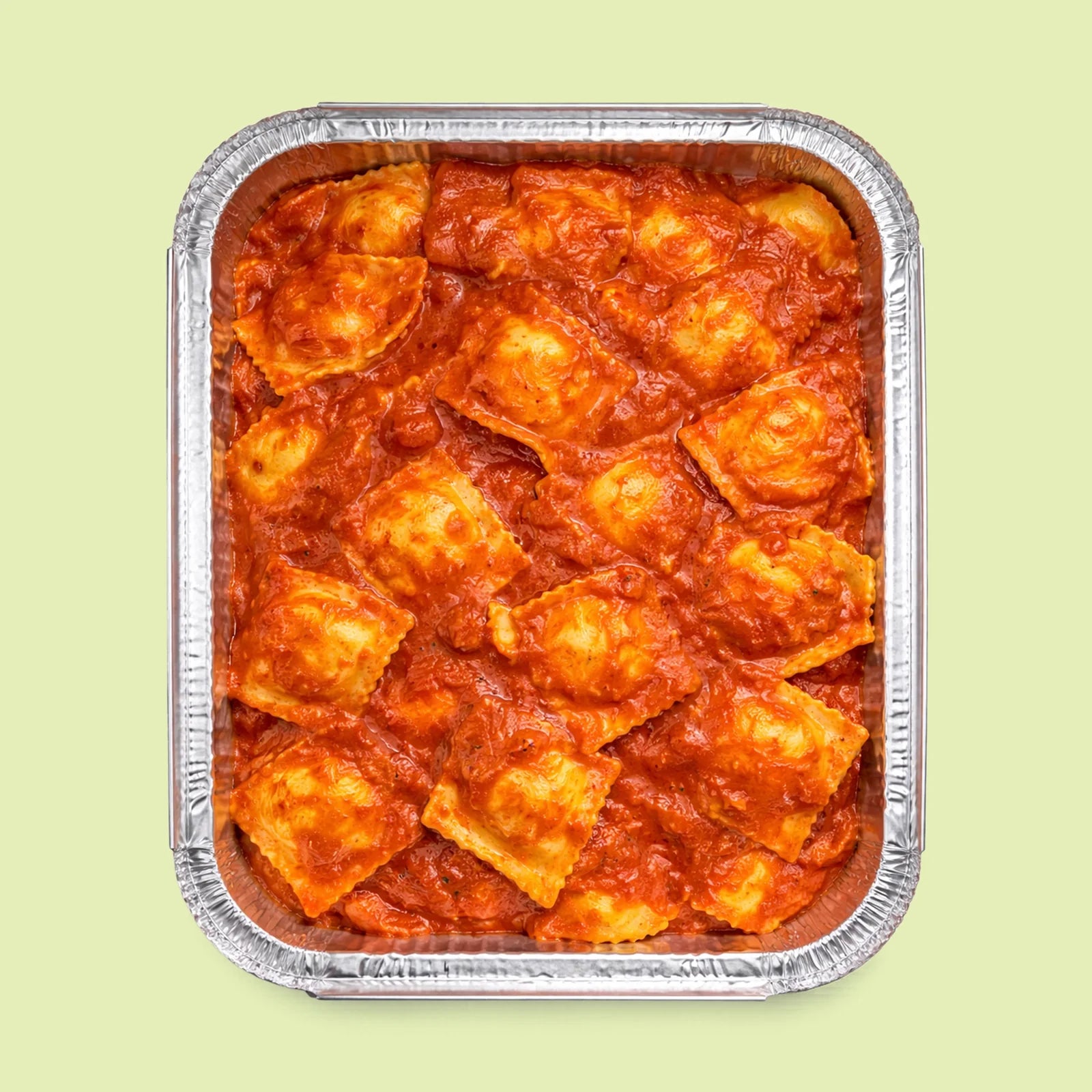 Aluminum foil container with ravioli pasta in a red tomato sauce on a light green background
