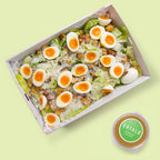 Box of salad with boiled eggs and croutons on a light green background, featuring the brand 'Eatalo'.